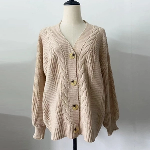 Close-up of beige chunky knit cardigan showing thick cable pattern and amber buttons
