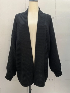 Detailed close-up of black knit cardigan texture with ribbed cuffs on gray studio background