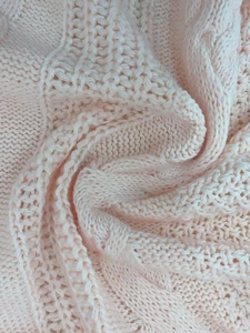 Detailed macro view of soft light pink cable knit pattern and texture on cardigan sweater