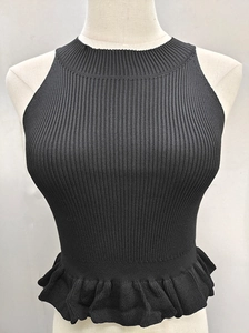 Detail of black ribbed knit crop top featuring ruffled peplum hem and halter neckline