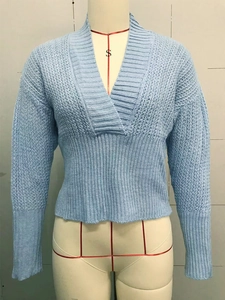 Detail of light blue knit sweater featuring deep V-neck and delicate hollow pattern