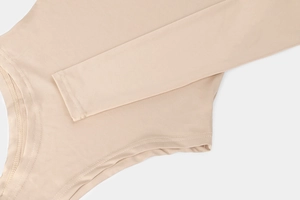 Detailed view of stitching and elastic fabric texture on a long-sleeve apricot bodysuit