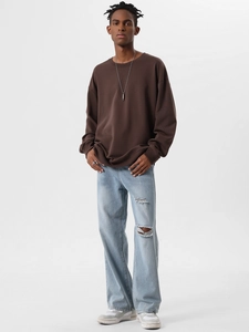 Male model in oversized dark brown crewneck sweatshirt with ripped blue jeans