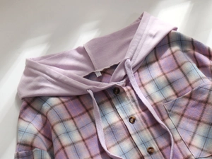 Detail of plaid hooded shirt in lilac and light blue featuring tortoiseshell buttons