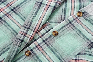 Close-up of pink and green plaid shirt fabric with amber buttons and detailed texture