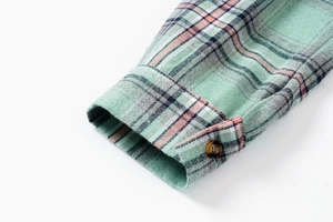Close-up of mint plaid flannel sleeve with a brown amber button and stitched cuff