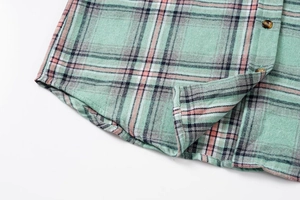 Detail of mint green plaid shirt featuring curved hem and amber textured buttons
