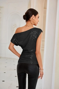 Detail of black sequined one-shoulder top showing shiny texture and ruched sleeve detail