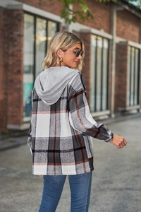 Outdoor street view of a women plaid hooded shirt jacket with grey knit hood and grey pattern