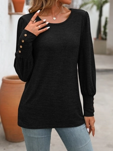 Close-up of elegant black crew neck top featuring gold button details on the sleeve cuffs