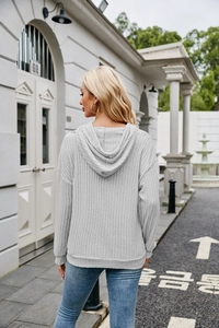 Outdoor street view showing the back of a light grey ribbed knit hoodie for women