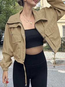 Detail of khaki cropped utility jacket showing metallic zipper and drawstring hem on street