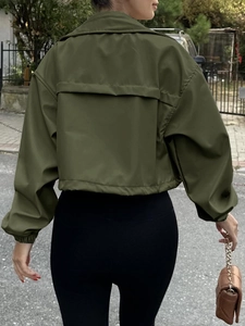 Back view of a cropped olive green windbreaker jacket with flap detail in outdoor street setting