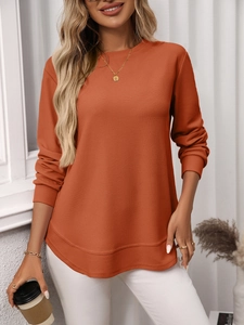 Detail of waffle knit fabric and layered curved hem on an orange long sleeve top