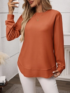 Close-up of orange waffle knit top featuring a curved layered hem and textured fabric