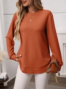 Detail of waffle knit fabric texture and curved layered hemline on long sleeve orange top