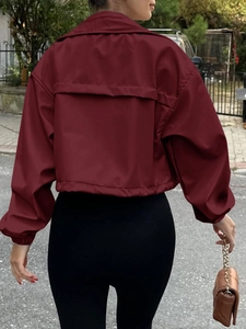 Rear view of a short burgundy zip-up windbreaker jacket with back storm flap and elastic cuffs