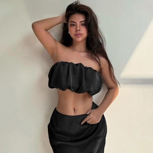 Detail of elegant black satin two-piece set featuring pleated off-shoulder top and slim skirt