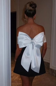 Detailed back view of a mini black dress featuring a large white satin bow detail