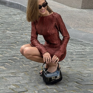 Détail d'une robe longue plissée rouge rouille avec tissu texturé et sac à main noir