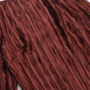 Détail de la texture d'un tissu plissé marron foncé avec un éclat satiné soyeux