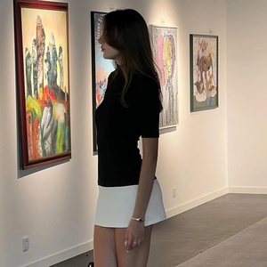 Donna elegante con top nero in maglia e minigonna bianca in una galleria d'arte