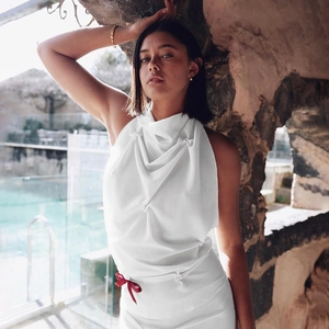 Detail of white halter neck top featuring draped neckline and a red bow accent