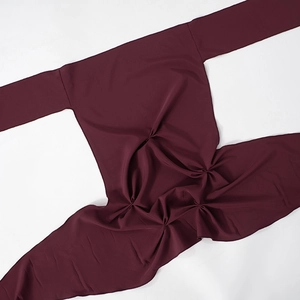 Detailed view of burgundy long sleeve top with textured waist pleats on white backdrop