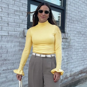 Close-up of the elegant ruffled cuffs and mock neck on this slim yellow long-sleeve top