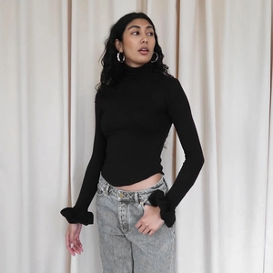Detail of elegant flared cuffs with ruffle decoration on a slim-fit black long-sleeve knit top