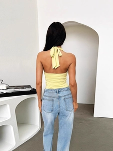 Top a lupetto giallo pallido con schiena scoperta e jeans azzurri in ambiente minimalista