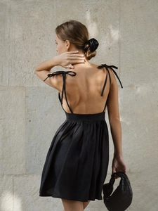 Detail of backless cotton dress featuring elegant bow straps and pleated waist design