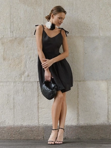 Detail of a black cotton backless dress with a V-neck and stylish braided leather handbag