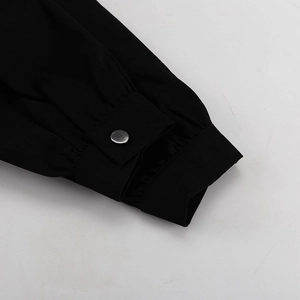 Close-up of pleated cuff on black dress featuring a single round silver metal button