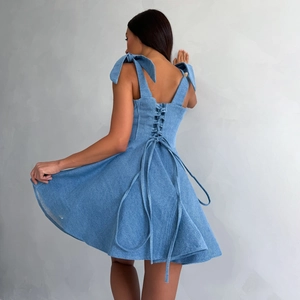 Detail van lichtblauwe denim jurk met vetersluiting op de rug en strikbandjes op schouders