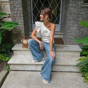 Detail of white one-shoulder ruffle top paired with blue wide-leg jeans and straw tote bag