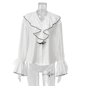 Close-up of V-neck white blouse featuring layered ruffles and black contrast piping detail
