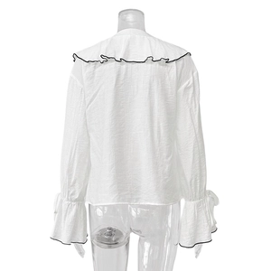 Detail of white ruffled lapel and flared sleeves with black contrast piping on the blouse