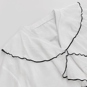 Detail of white blouse featuring layered ruffles and black contrast stitching on the collar