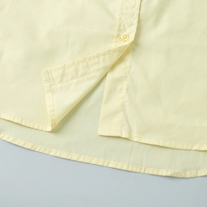 Close-up of a yellow cotton shirt detail showing hemline, button and fabric texture
