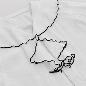 Close-up of white French style blouse featuring chic black ruffled edges and texture