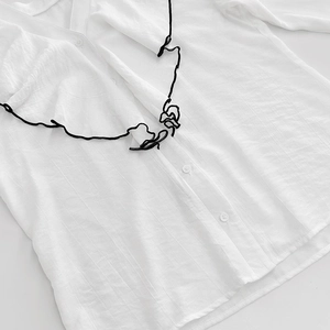 Detail of white V-neck shirt featuring black abstract embroidery and striped texture