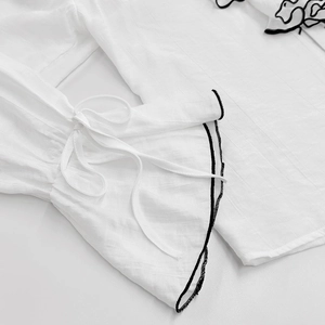 Detail of white bell sleeves with black piping and tie ribbon on textured woven fabric