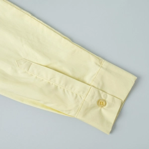 Close-up of yellow cotton shirt cuff with neat stitching and matching resin button