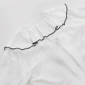 Close-up of ruffled lapel collar on white cotton shirt with black contrast piping