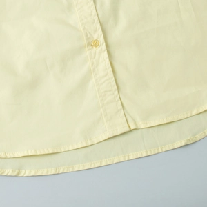 Detailed macro view of the curved hem and double stitching on yellow cotton shirt