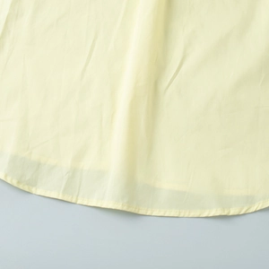 Detailed close-up of the fine stitching and breathable cotton fabric on yellow shirt hem