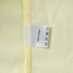 Detail view of cotton shirt fabric texture with wash care label showing 100% Cotton