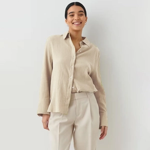 Detail shot of the crinkled cotton fabric and buttoned cuff on the light beige shirt