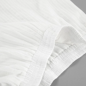 Close-up of white jacquard cotton fabric with vertical stripe texture and elastic waistband detail